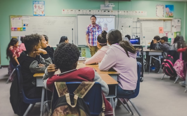 A teacher standing in front of a class of children who are sitting at desks.